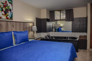Een hotelkamer met een groot bed, een kitchenette, een badkamer en een schilderij aan de muur.