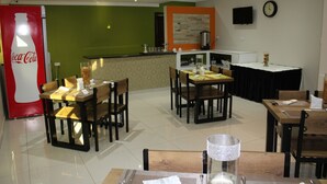 Un espace repas avec plusieurs tables et chaises, un réfrigérateur Coca-Cola, une machine à café et un téléviseur fixé au mur.