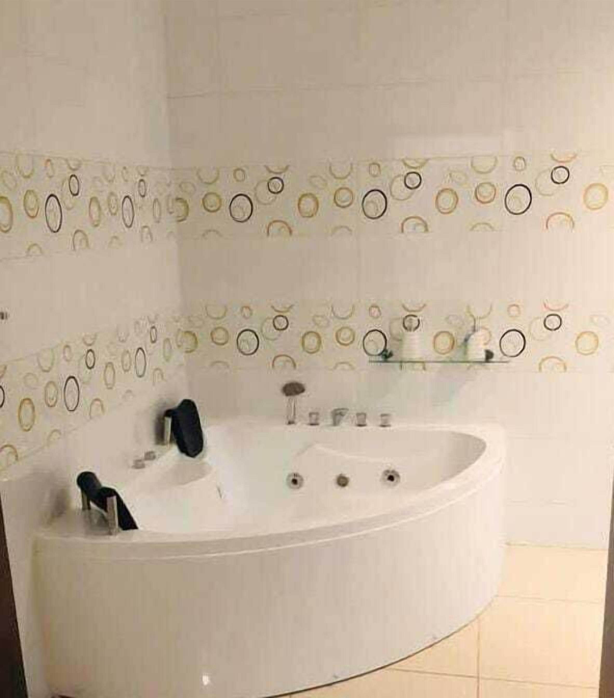 A bathroom with a white bathtub, a mirror, and a wall with circular patterns.