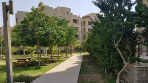A pathway lined with trees and a picnic table, leading to a building with multiple balconies. - The Village Luxury Suites (New Cairo)