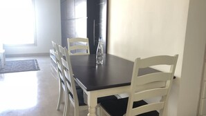 A dining area with a dark wooden table, white chairs, and a clear bottle on the table. - The Village Luxury Suites (New Cairo)
