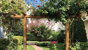 A garden pathway with a wooden pergola, surrounded by lush greenery and flowering plants. - Central Plaza Studio (Sunny Beach)