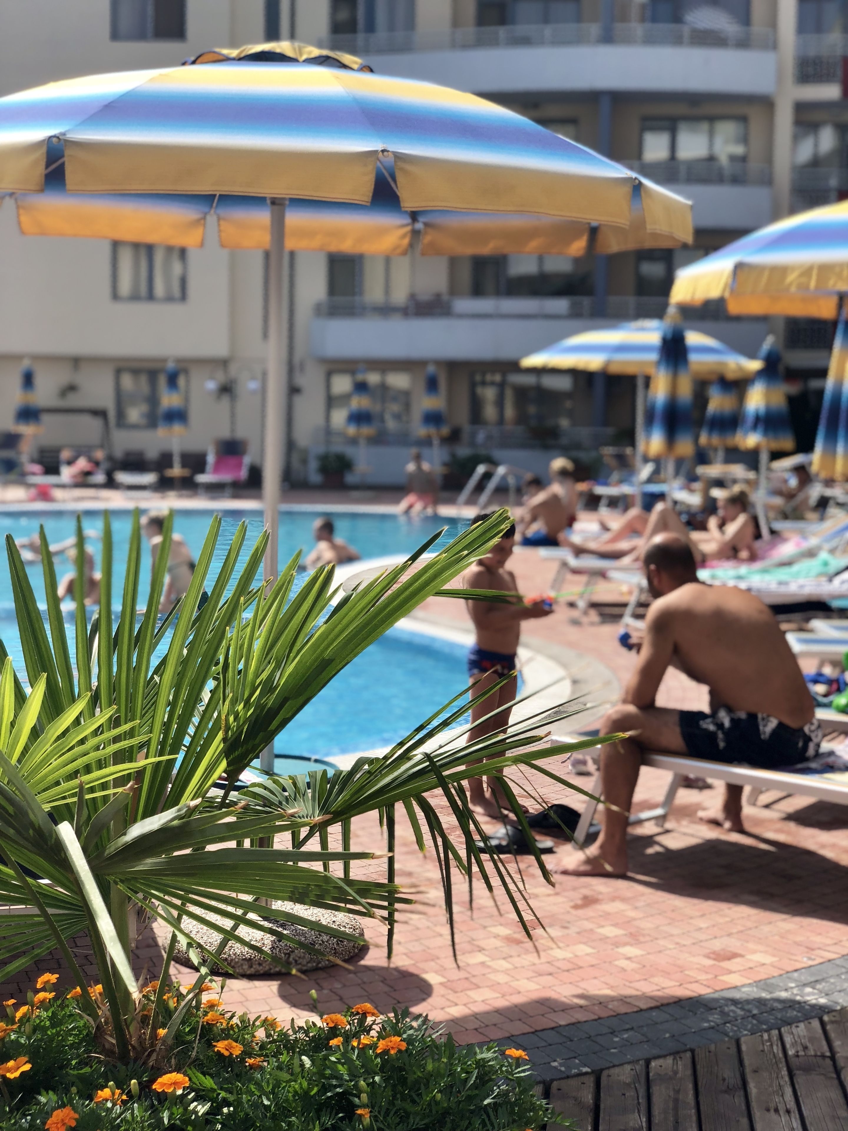 A pool area with multiple umbrellas, lounge chairs, and people relaxing by the pool.