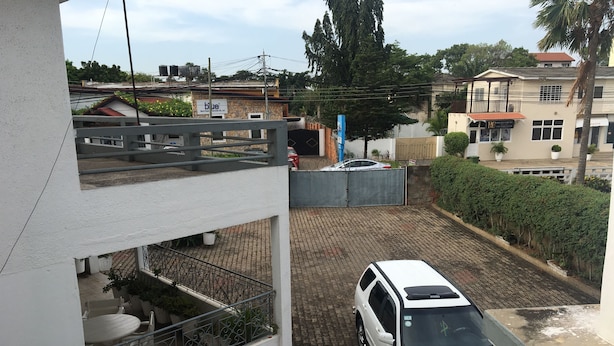 Un SUV blanco estacionado en un camino de entrada pavimentado con un acceso vigilado, rodeado de plantas en macetas y un balcón con mobiliario exterior.