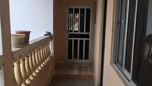 Un pasillo con piso de baldosas, una puerta blanca con reja metálica y una ventana a la derecha.