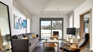 Ein modernes Wohnzimmer mit Sofa, Couchtisch und Fernsehsessel. An der Wand befindet sich ein Fernseher und ein Gemälde.