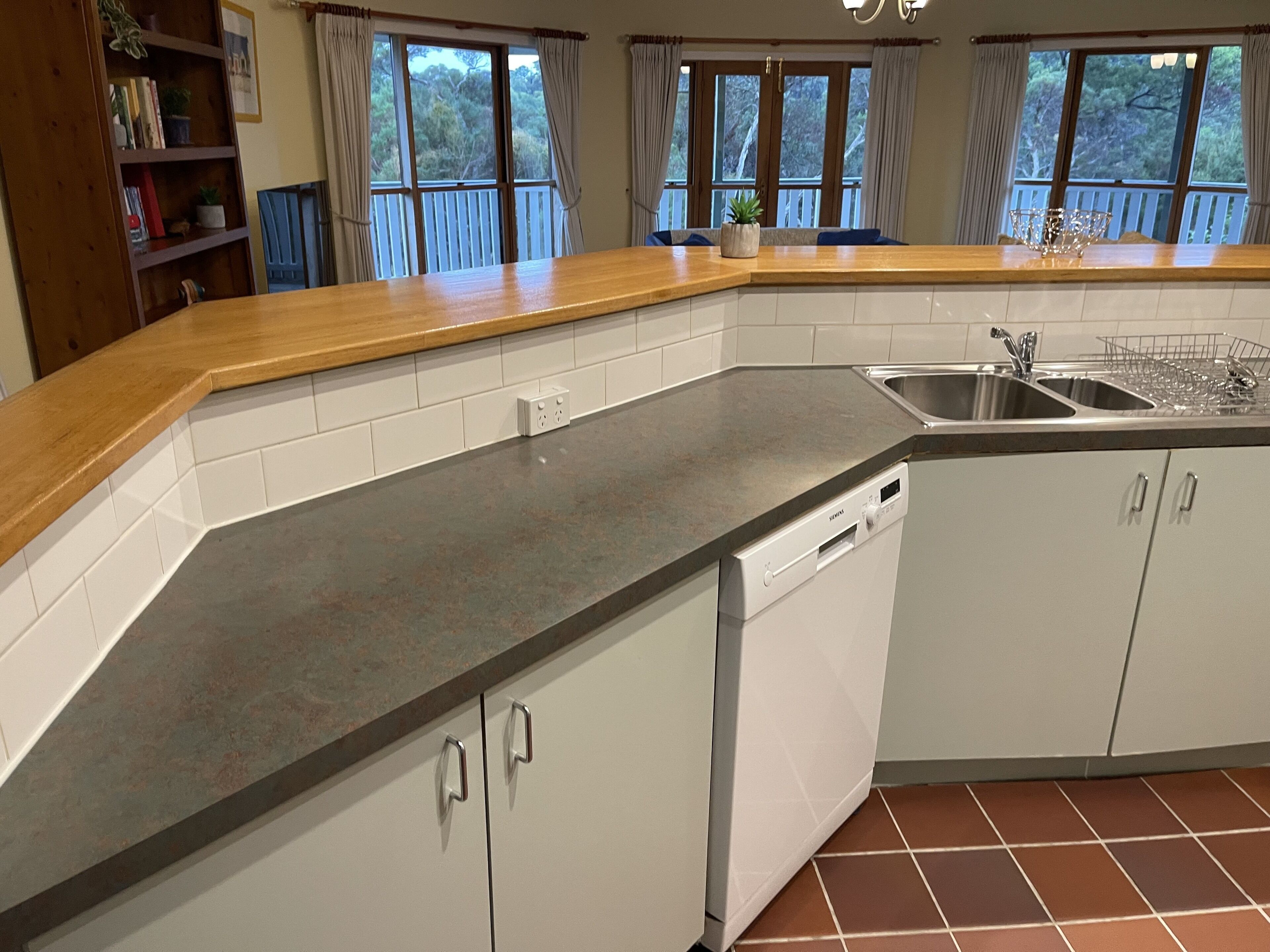 A kitchen with white cabinets, a granite countertop, a dishwasher, and a window with a view of trees.