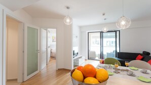 Ein modernes Wohnzimmer mit Essbereich, mit Obstschale, Esstisch und Sitzgelegenheiten.