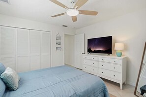 A bedroom with a bed, a dresser, a ceiling fan, a TV, and a night sky painting.