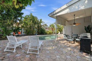 A backyard with a swimming pool, lounge chairs, a ceiling fan, and a barbecue grill.