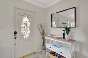 A white door with a stained glass window, a white console table with a mirror above it, and a vase with a plant.