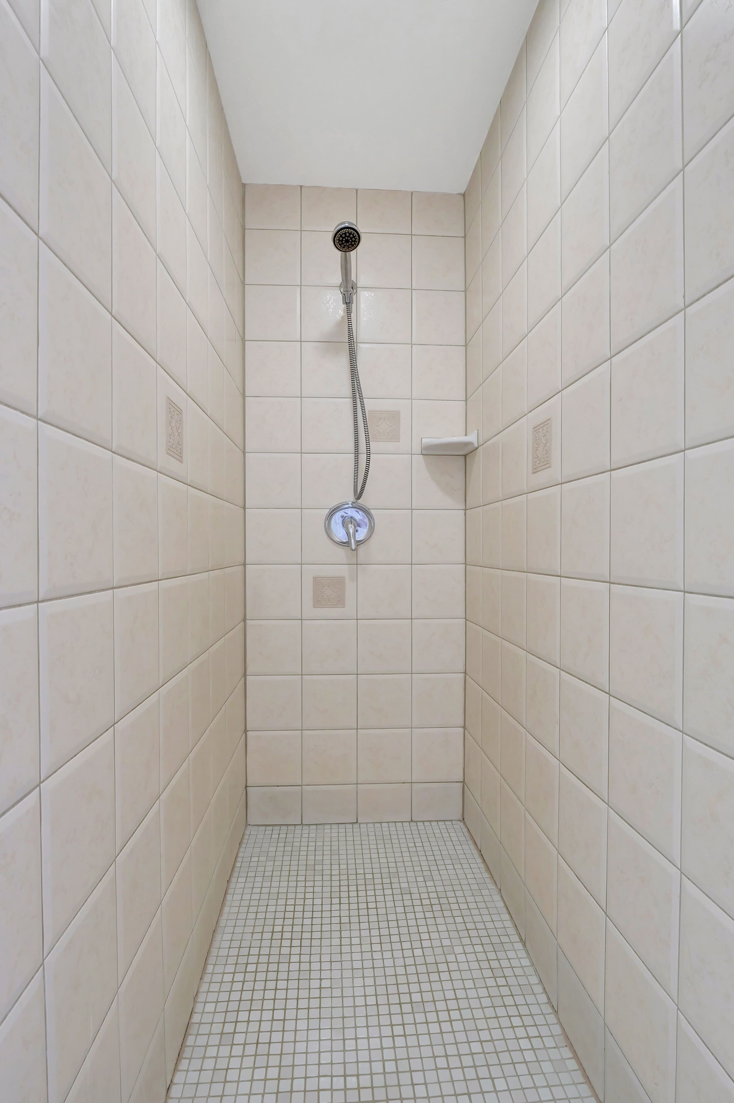 Un piccolo bagno con rivestimento piastrellato, doccetta a mano e rubinetto montato a parete.