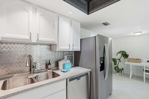 A modern kitchen with white cabinets, a stainless steel sink, a dishwasher, and a refrigerator.