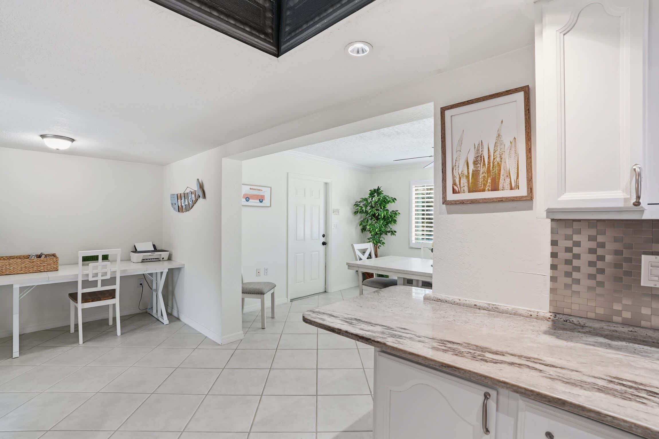 Una cocina moderna con armarios blancos, encimera de mármol y una zona de comedor con mesa y sillas blancas.