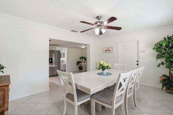 A dining area with a white table, white chairs, a ceiling fan, and a door.