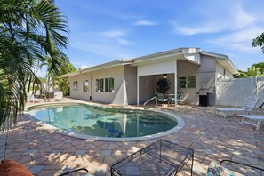 A modern house with a swimming pool, patio furniture, and a barbecue area.