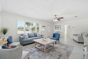 A spacious living room with a light-colored sofa, a blue armchair, and a coffee table.