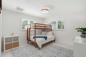 A bunk bed in a room with white walls, a white ceiling, and a patterned rug.