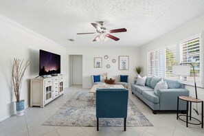 A living room with a TV, sofa, coffee table, and ceiling fan.