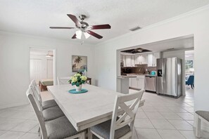 A modern kitchen with stainless steel appliances, a dining area with a white table and grey chairs, and a ceiling fan.