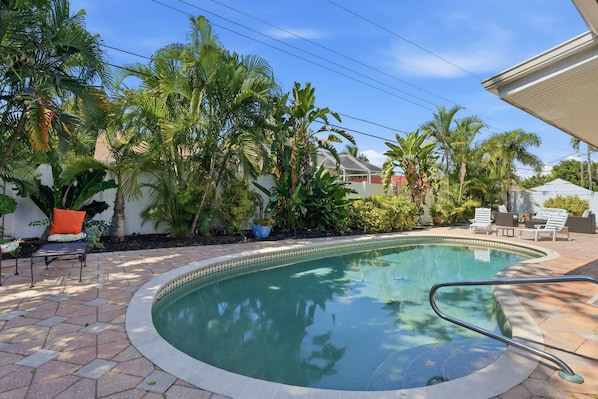 A swimming pool with a tiled deck, surrounded by palm trees and a white fence.