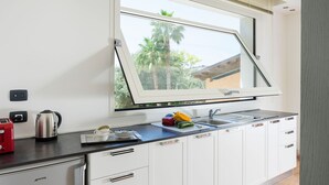A modern kitchen with a large window, white cabinets, a stainless steel kettle, and a red toaster.