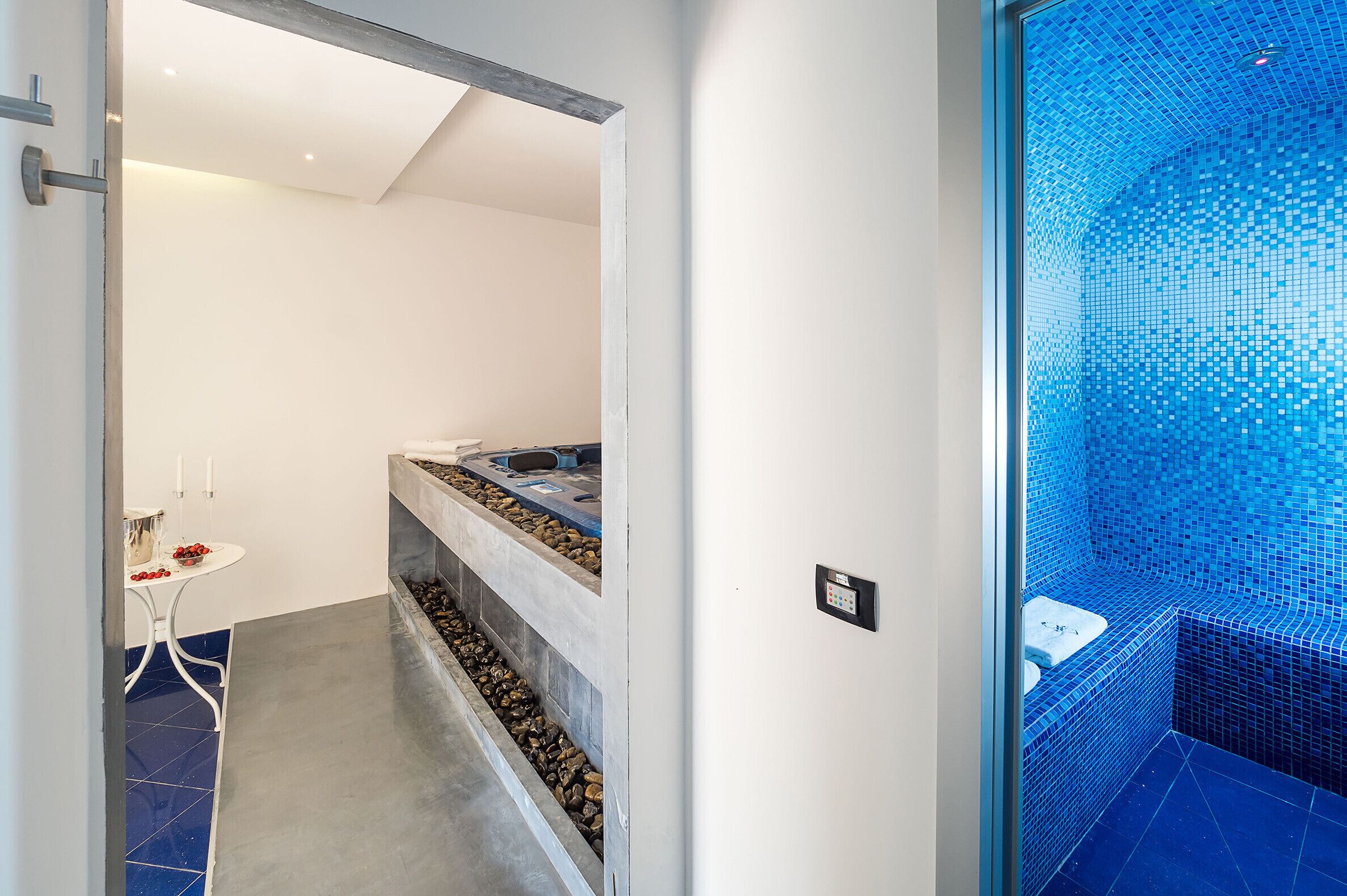 Un bagno moderno con parete in mosaico blu, una panca integrata e un piccolo tavolo con un vaso.