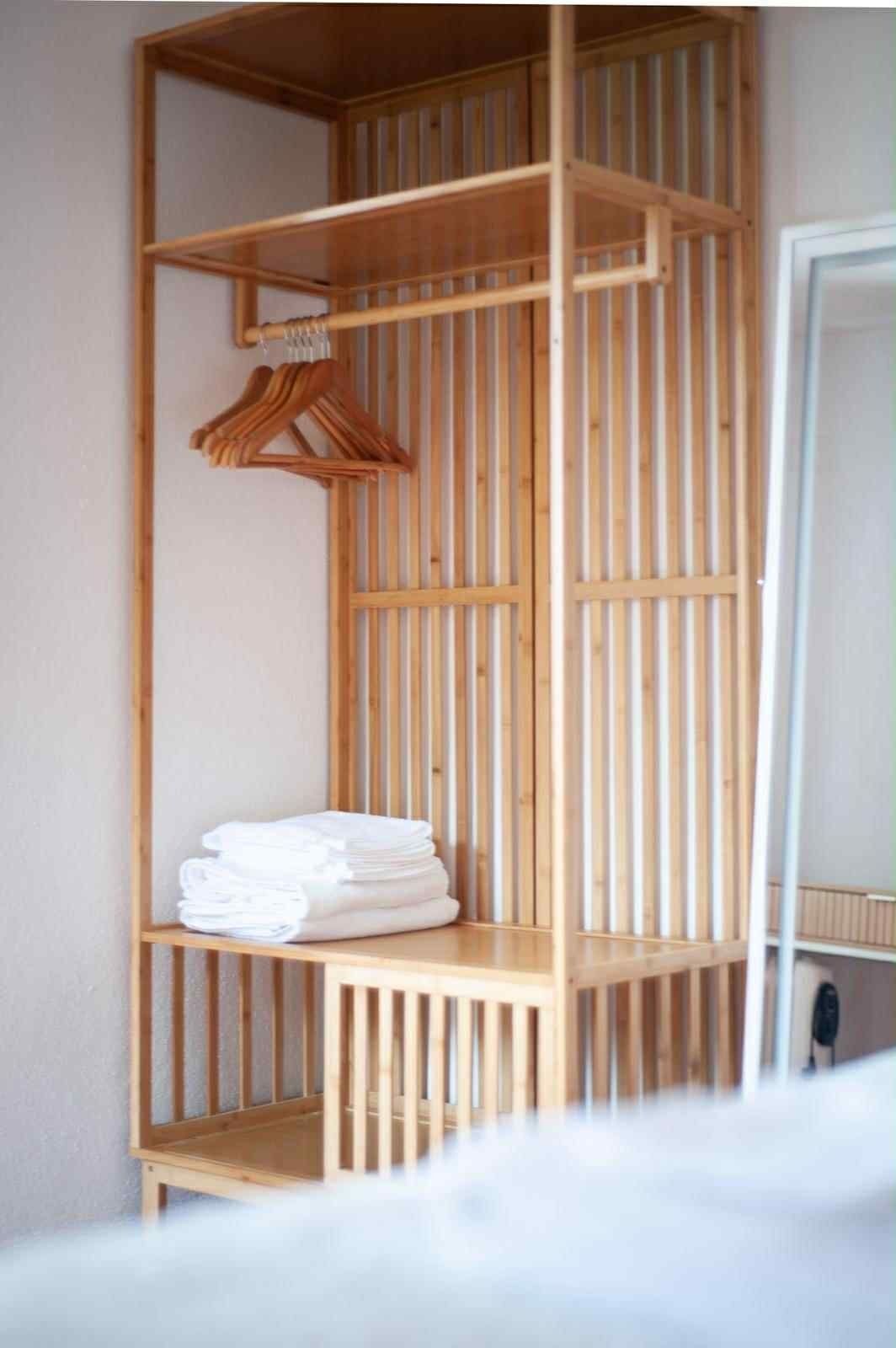 Un armario de madera con varias repisas y una barra para colgar, que contiene toallas blancas dobladas.