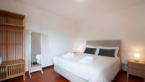 Una camera d'hotel con un letto grande, un armadio in legno, uno specchio a figura intera e lampade ai comodini.
