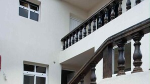 Un edificio con facciata bianca, una scala in legno con balaustre e numerosi vasi con piante disposti lungo i gradini.