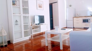Een moderne woonkamer met een televisie, witte meubels, een eettafel en een keukenhoek met een magnetron.