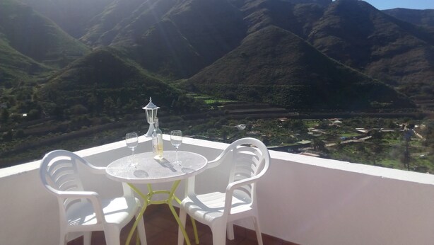 Een tafel met twee stoelen en een fles op een balkon met uitzicht op een bergachtig landschap.