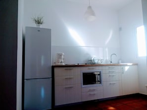 Cozinha moderna com armários brancos, forno embutido, cafeteira e luminária pendente.