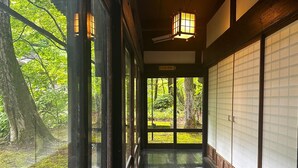 Une pièce de style japonais traditionnel, avec un sol recouvert de tatamis, des portes coulissantes et une vue sur une zone boisée.