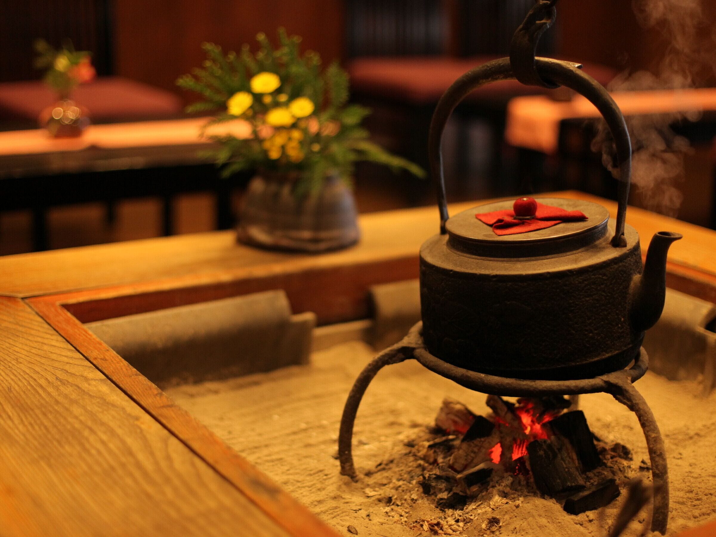 A traditional tea kettle on a sand-filled tray with a fire underneath, set in a cozy indoor environment.