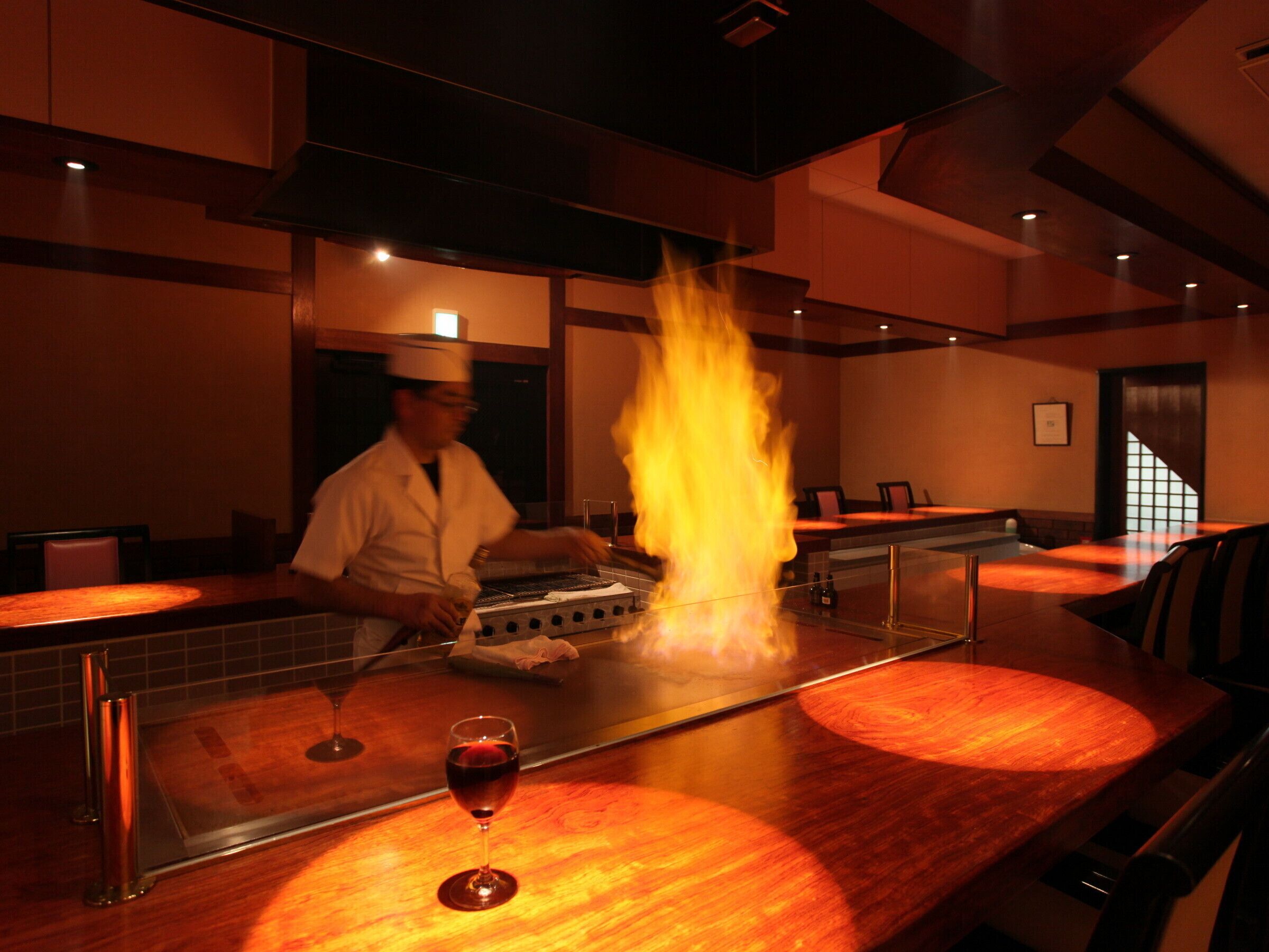 A chef cooking with flames on a grill in a restaurant setting.