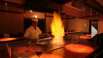 A chef cooking with flames on a grill in a restaurant setting.