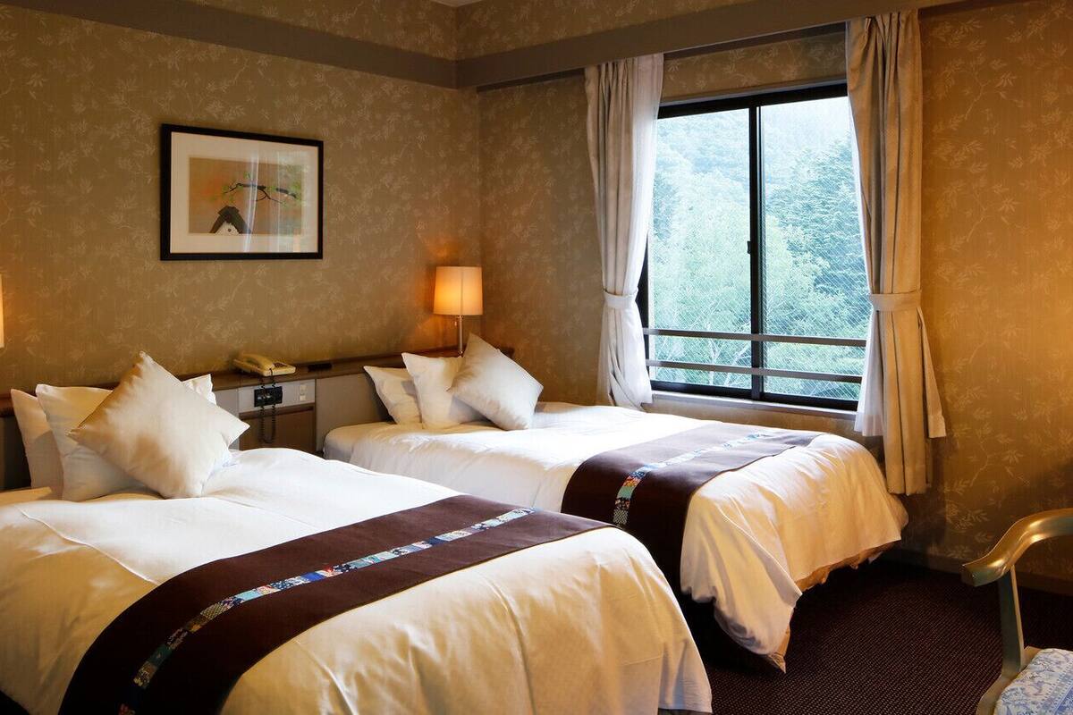 Une chambre d’hôtel avec deux lits, un bureau, une chaise, une fenêtre avec des rideaux et un tableau encadré au mur.