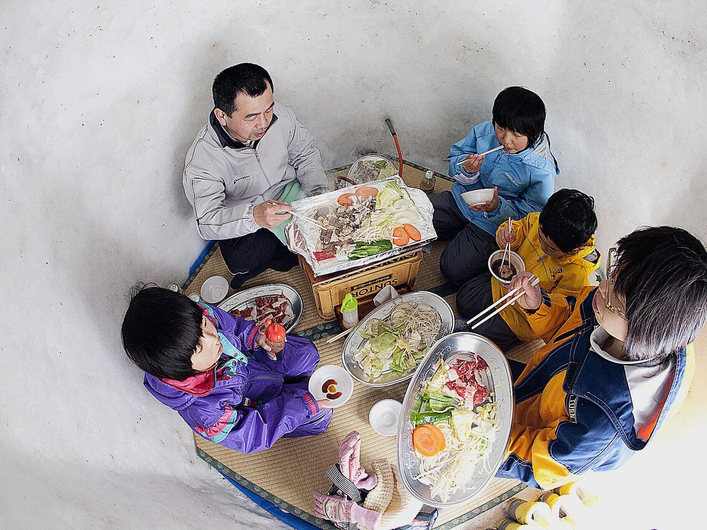 A group of people sitting around a table with various dishes, indicating a communal meal setting.