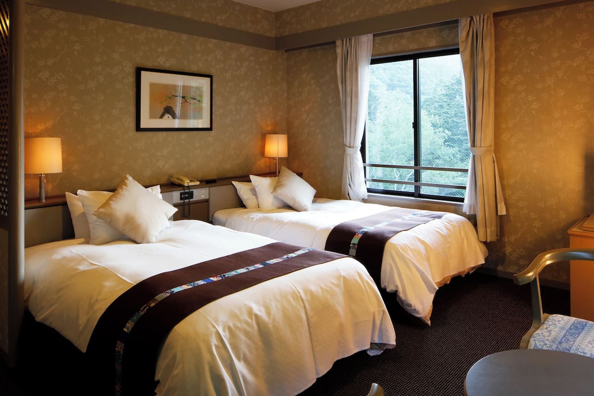 Une chambre d’hôtel avec deux lits, un bureau, une chaise et une fenêtre avec des rideaux.