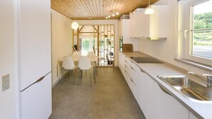 A modern kitchen with white cabinets, a stainless steel sink, and a dining area with white chairs. - 2 bedroom pet friendly home in Broager (Broager)