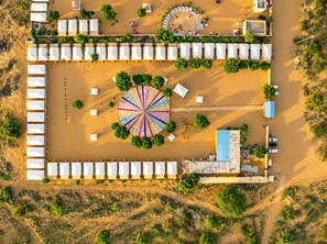 Eine Luftaufnahme eines Resorts mit mehreren weißen Zelten, die in Reihen angeordnet sind, einem zentralen, kreisförmigen Bereich mit farbigen Linien und einigen Bäumen.