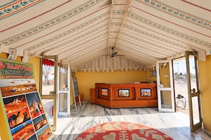 A tented room with a reception desk, a poster on the wall, and a view of the desert outside.
