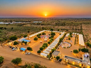 An aerial view of a resort with multiple tents and a central building, surrounded by open fields and sparse vegetation.