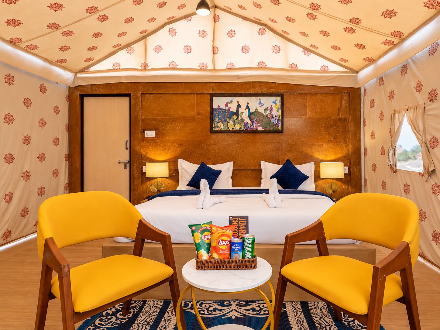 Una habitación de hotel con cama, dos sillones, una mesita con aperitivos y un cuadro en la pared.