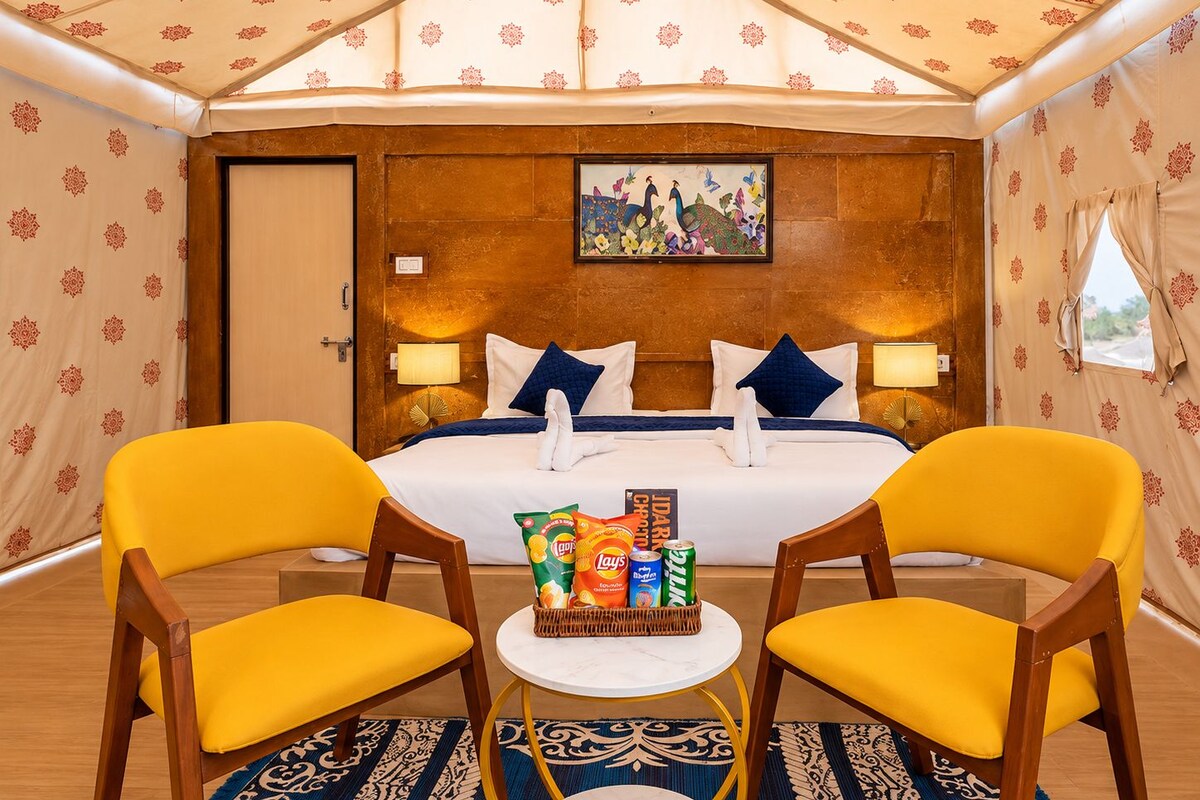 Ein Hotelzimmer mit Bett, zwei Stühlen, einem kleinen Tisch mit Snacks und einem Bild an der Wand.
