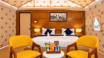 Una habitación de hotel con cama, dos sillones, una mesita con aperitivos y un cuadro en la pared.