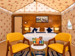 Ein Hotelzimmer mit Bett, zwei Stühlen, einem kleinen Tisch mit Snacks und einem Bild an der Wand.