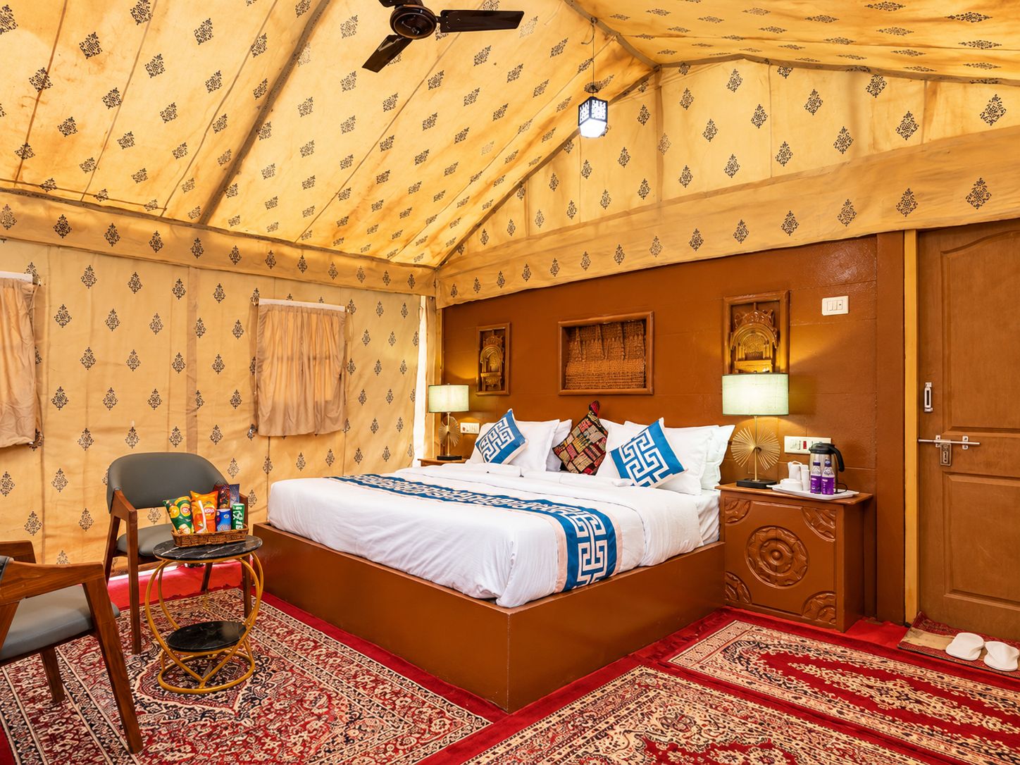 A room with a bed, a chair, a small table, a nightstand, and a door.