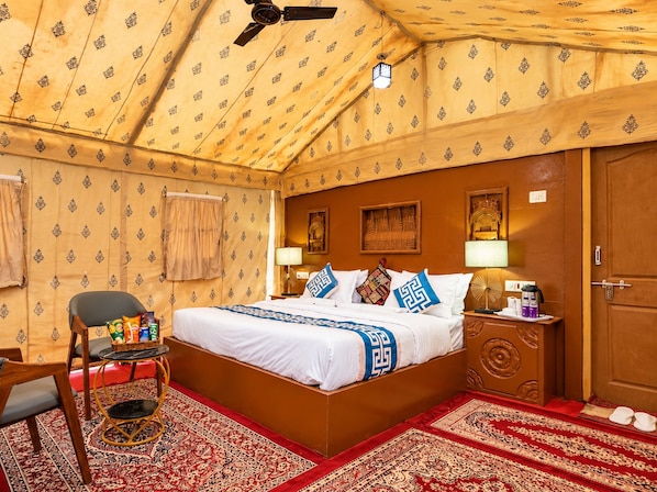 A room with a bed, a chair, a small table, a nightstand, and a door. - Rajputana Desert Camp By Castle Crown (Jaisalmer)